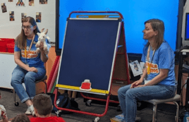 Two librarians speak to preschoolers in their classroom about summer reading.