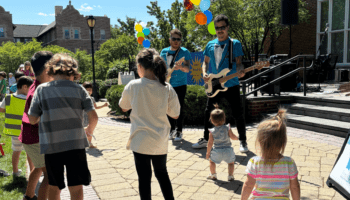 Kids and toddlers dance while members of a band perform holding guitars