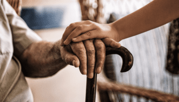 photo of younger hand on top of elderly hand resting on cane